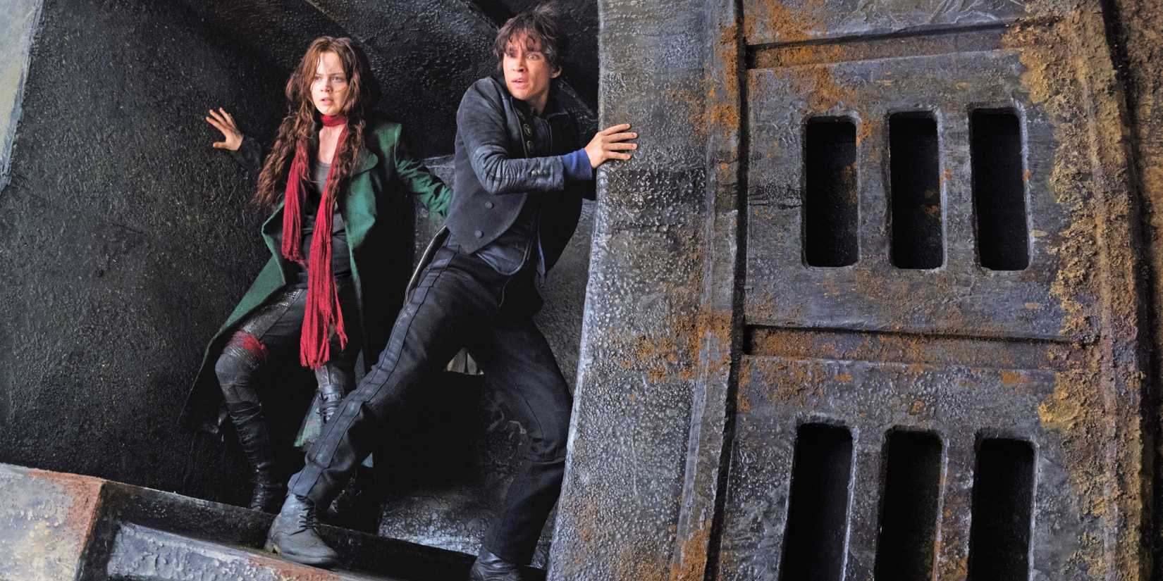 Two young resistance fighters stands in a large metal structure, looking down at something with dread.