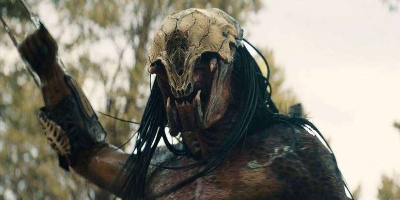 The Predator holds its hand up in a fist in the forest in Prey