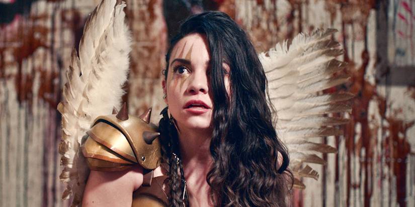 Lauren LaVera as Sienna wearing a warrior costume with angel wings infront of a bloody warehouse-like background in Terrifier 2 (2022)