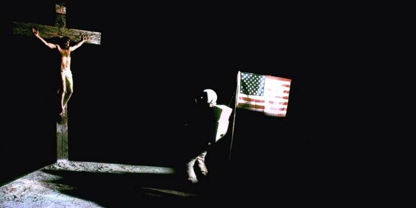 An astronaut holding the US flag in front of a crucifix in The Ninth Configuration
