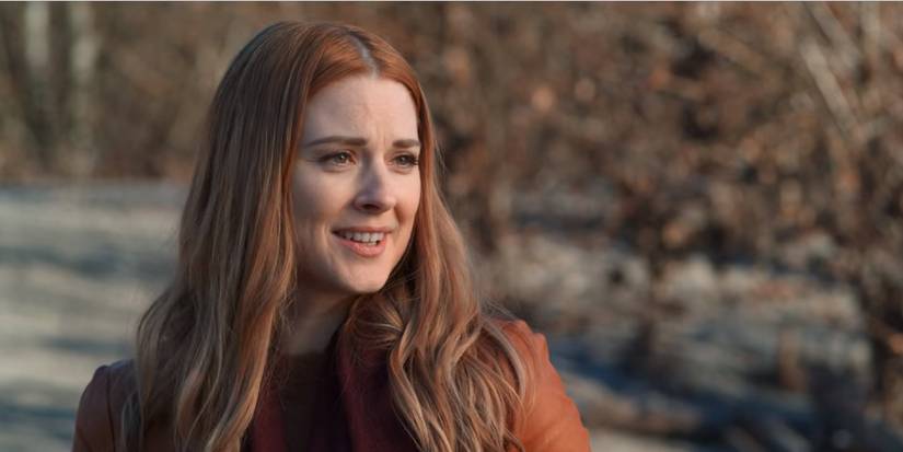 A woman looks at something off camera in front of trees in Virgin River.
