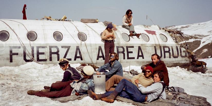 The cast of Society of the Snow sitting beside a crashed plane