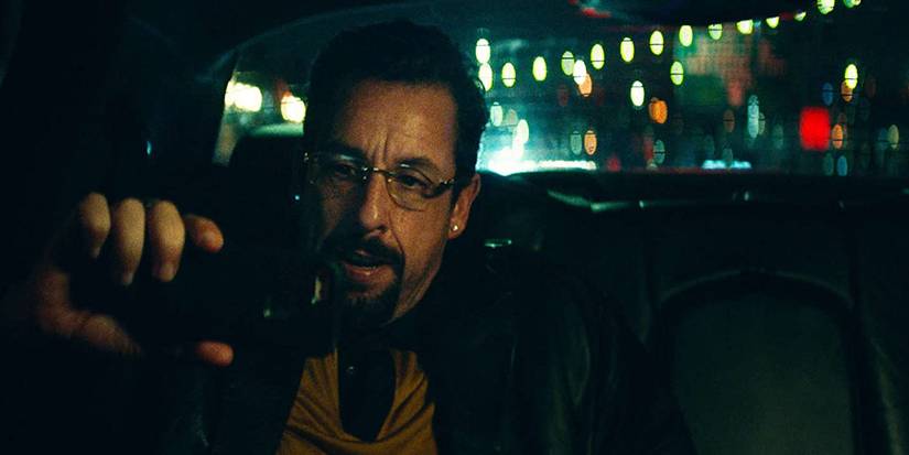 Howard Ratner sits in a car and watches a basketball game on his phone.