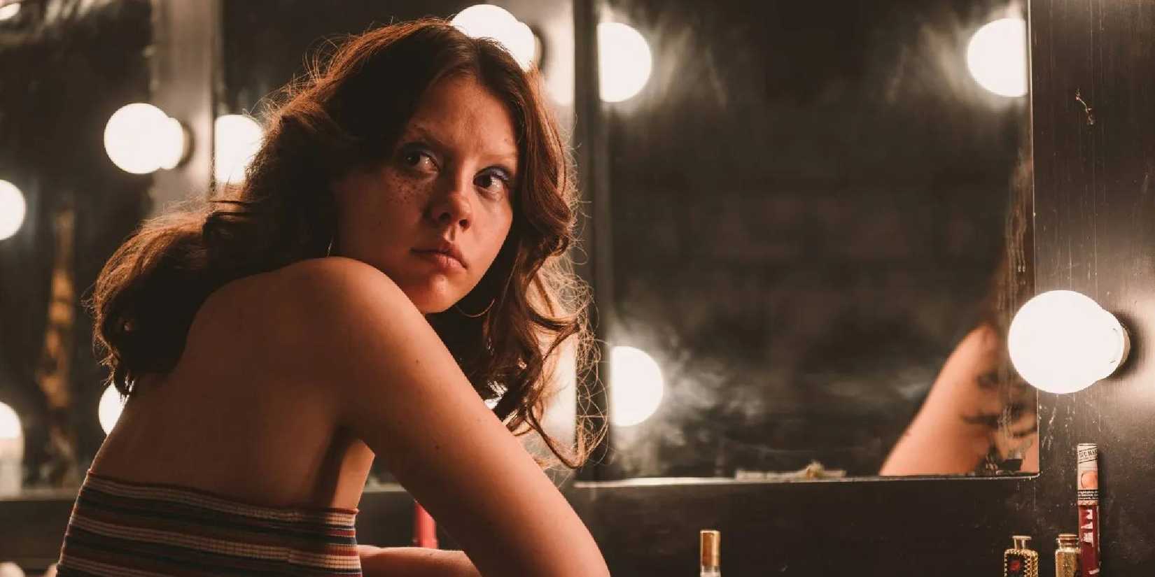 Mia Goth as Maxine sitting in front of a mirror looking over her shoulder in X.
