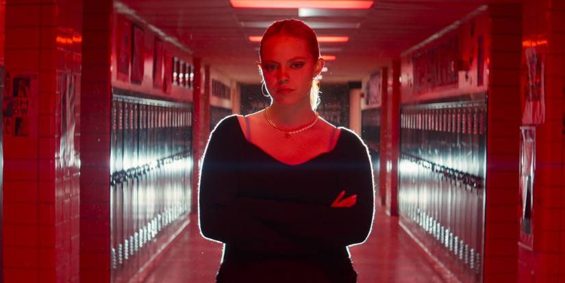 Renee Rapp as Regina George standing in the high school hallway with red overhead lights in Mean Girls