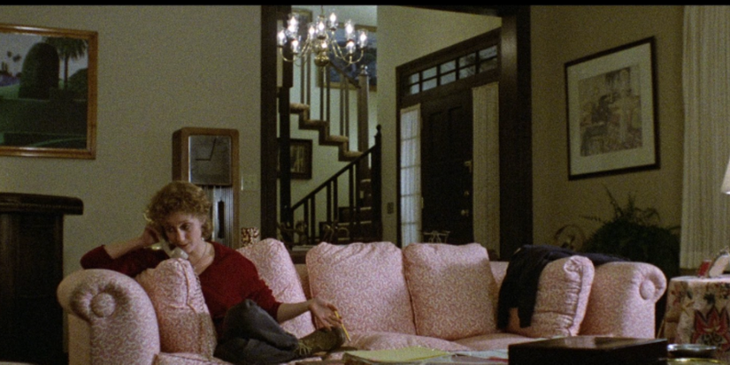 Carol Kane as Jill Johnson sitting on a pink couch and holding a phone in a red sweater in When A Stranger Calls