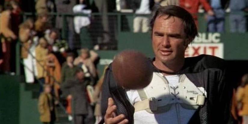 Paul Crewe, portrayed by Burt Reynolds, plays with football while playing in a stadium