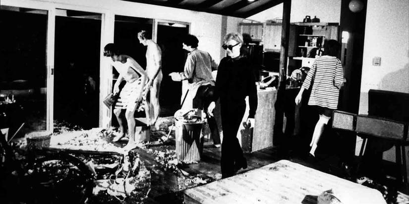 Andy Warhol caminhando por uma sala com homens sem camisa no backgroun em quatro estrelas 1