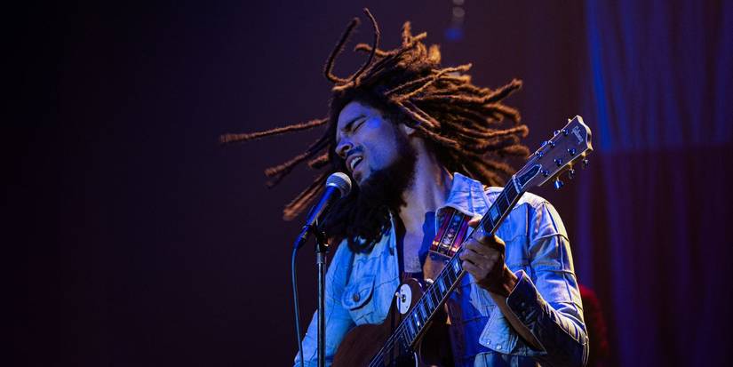 Bob Marley (Kingsley Ben-Adir) performing on the stage with a guitar in Bob Marley: One Love.