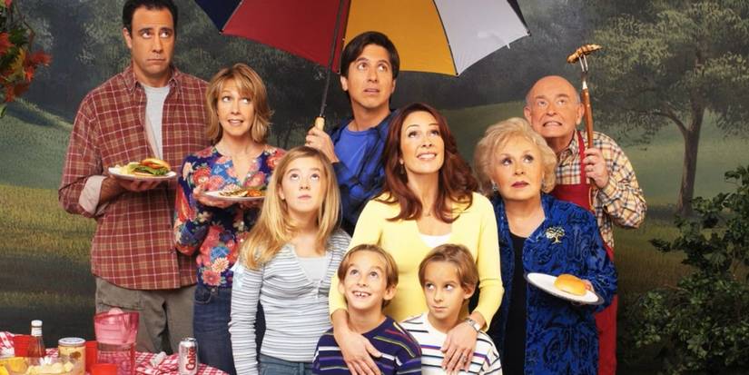 The cast look upwards under an umbrella at a rainy picnic in a promo photo for Everybody Loves Raymond.