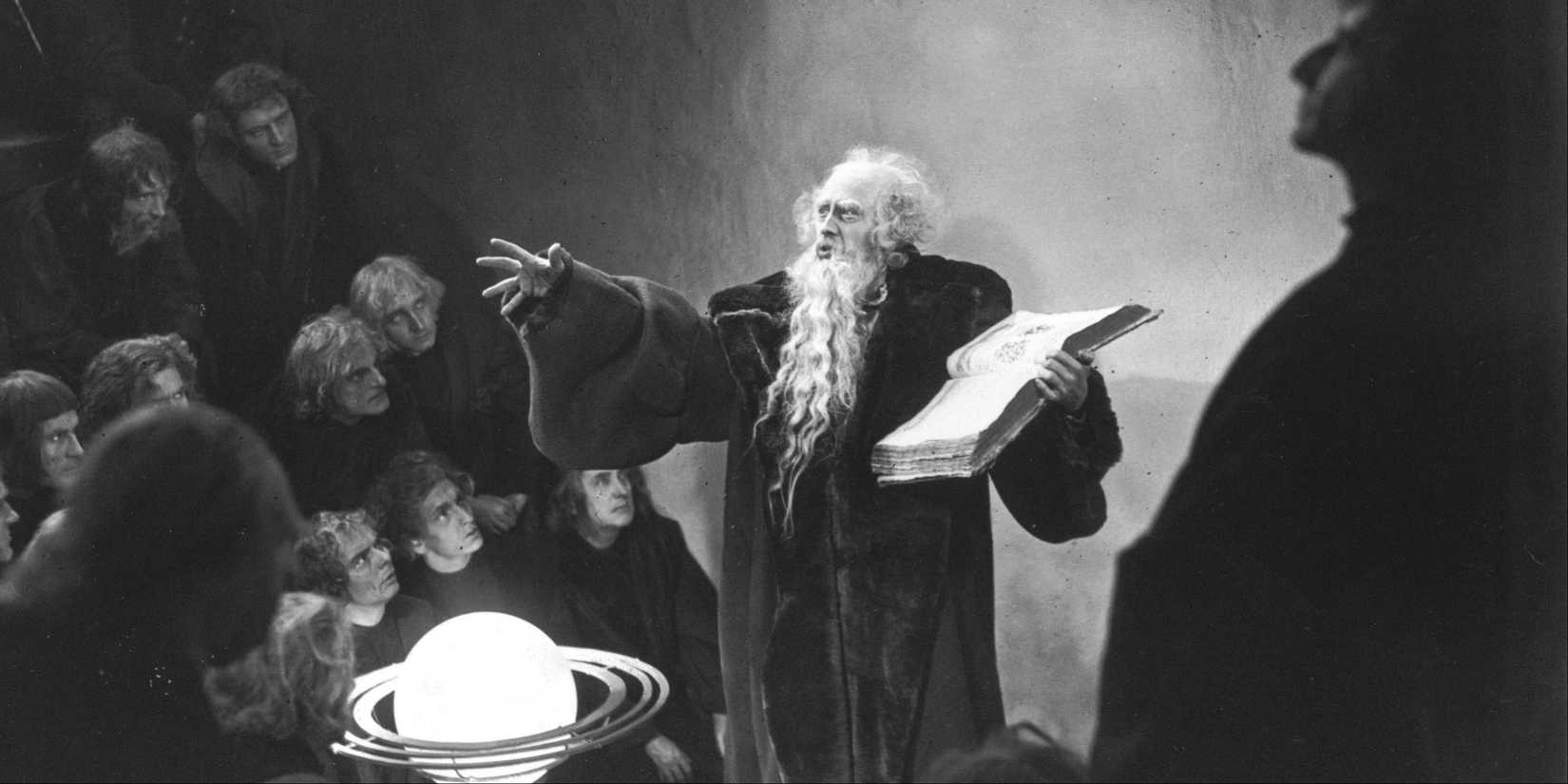 Gösta Ekman as Faust holding a book talking to a room of people in Faust