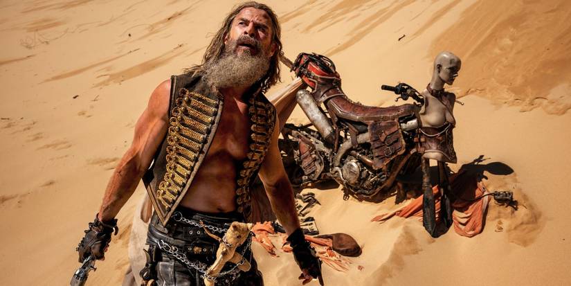 Chris Hemsworth sebagai Panglima Perang Dementus di Furiosa: A Mad Max Saga berdiri di bukit pasir. 