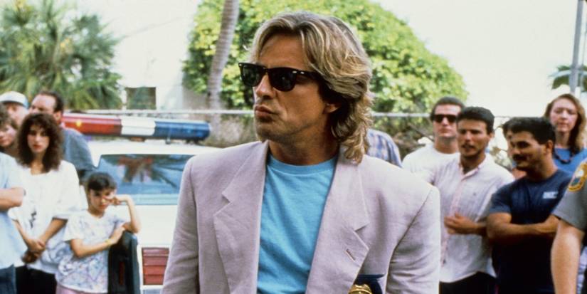 Don Johnson as James Crockett in Miami Vice standing in a crowd with a white blazer, blue T-shirt, and sunglasses.
