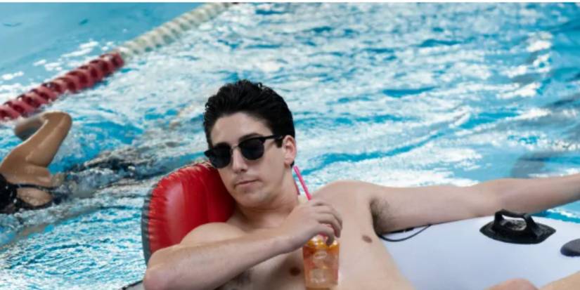 Milo Manheim as Wally drinks from a straw while in an innertube in the pool in School Spirits