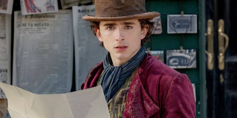Timothee Chalamet as a young Willy Wonka holding a newspaper and looking stunned in Wonka