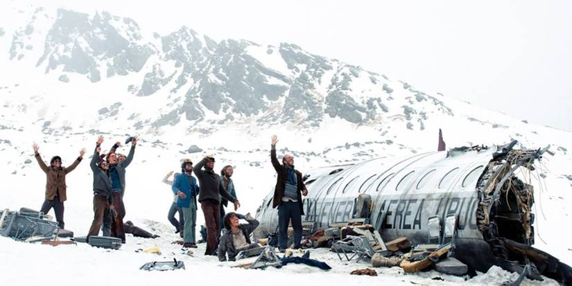 A group of men waving at the sky next to a plane wreckage in a snowy mountain in Society of the Snow (2023)