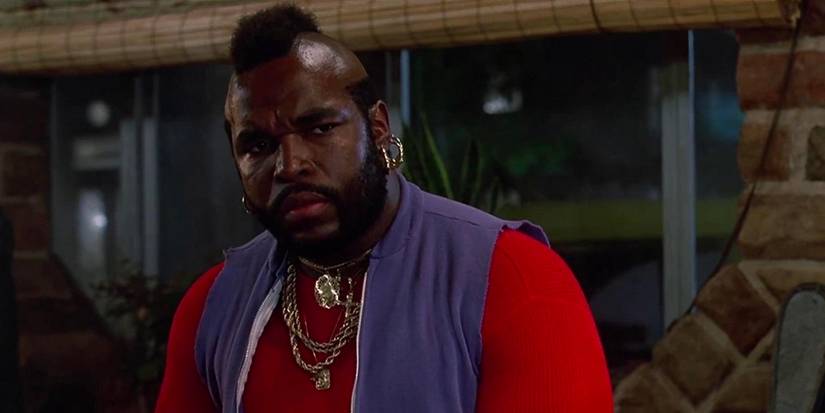 Mr. T scowls while wearing a bright red shirt and a blue vest and plenty of his trademark jewelry.
