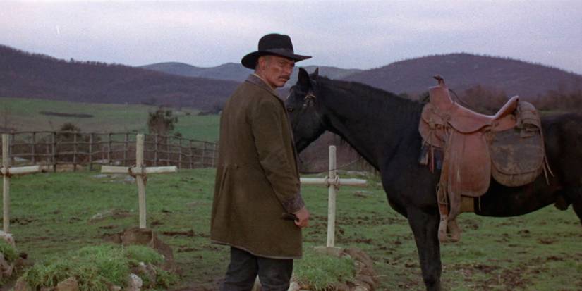 Lee Van Cleef as Ryan tends to his horse while peering over his shoulder in a fresh graveyard in Death Rides a Horse