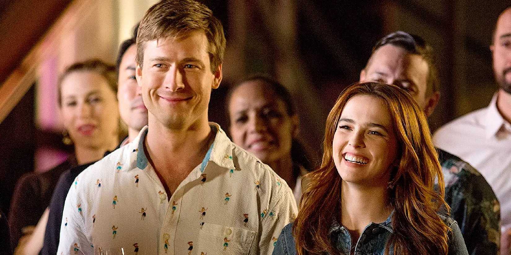Glen Powell and Zoey Deutch as Charlie and Harper, smiling and standing side by side Set It Up.