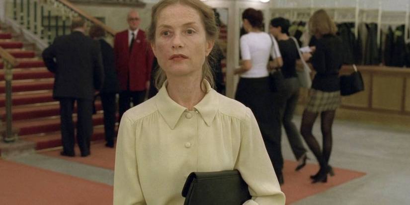 Erika standing in a lobby looking intently as if searching for someone in The Piano Teacher