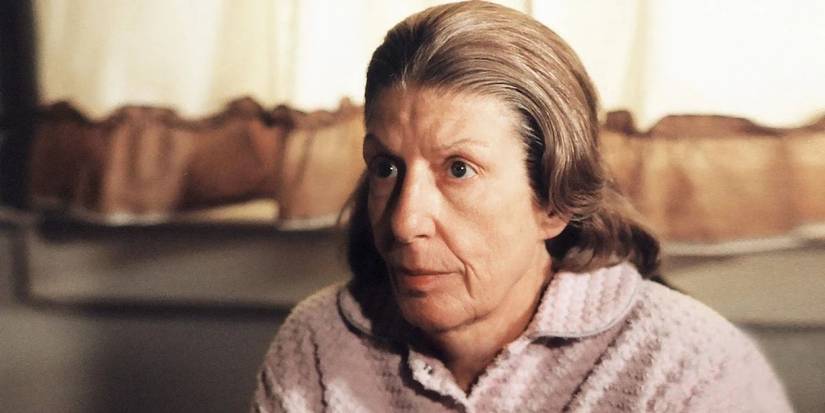 Livia Soprano sits in front of a window with curtains and looks serious in The Sopranos.