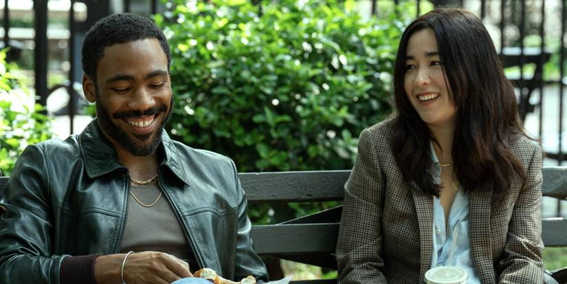 Donald Glover and Maya Erskine sitting on a park bench and laughing in Mr. & Mrs. Smith