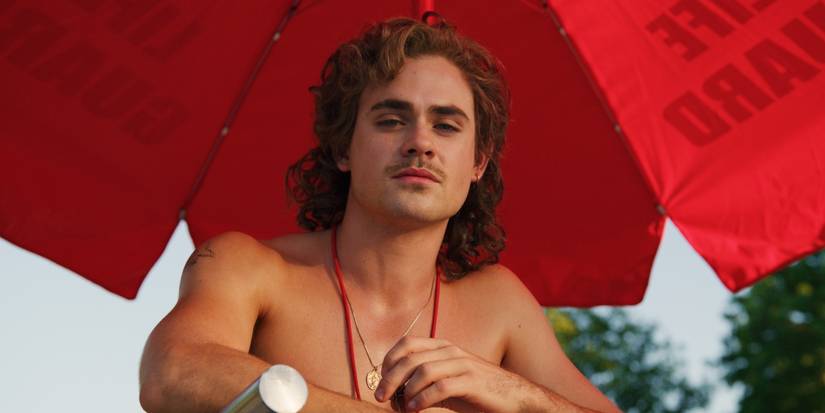 Dacre Montgomery as Billy shirtless, sitting in a lifeguard chair and looking down in Stranger Things.