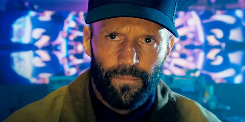 Adam Clay rolünde Jason Statham, arıcıdaki ekrandan bir kişiye bakarken