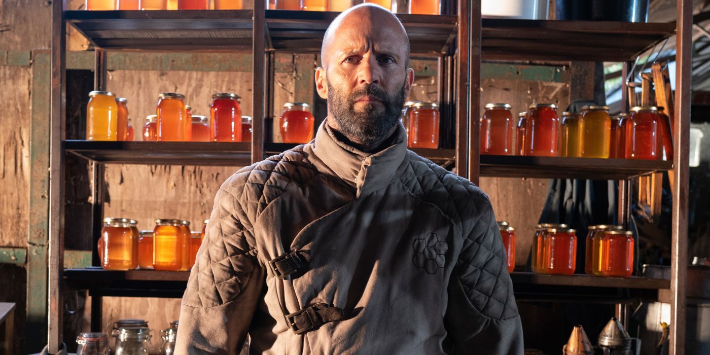 Jason Statham as Adam Clay, standing in front of jars of honey, in The Beekeeper.
