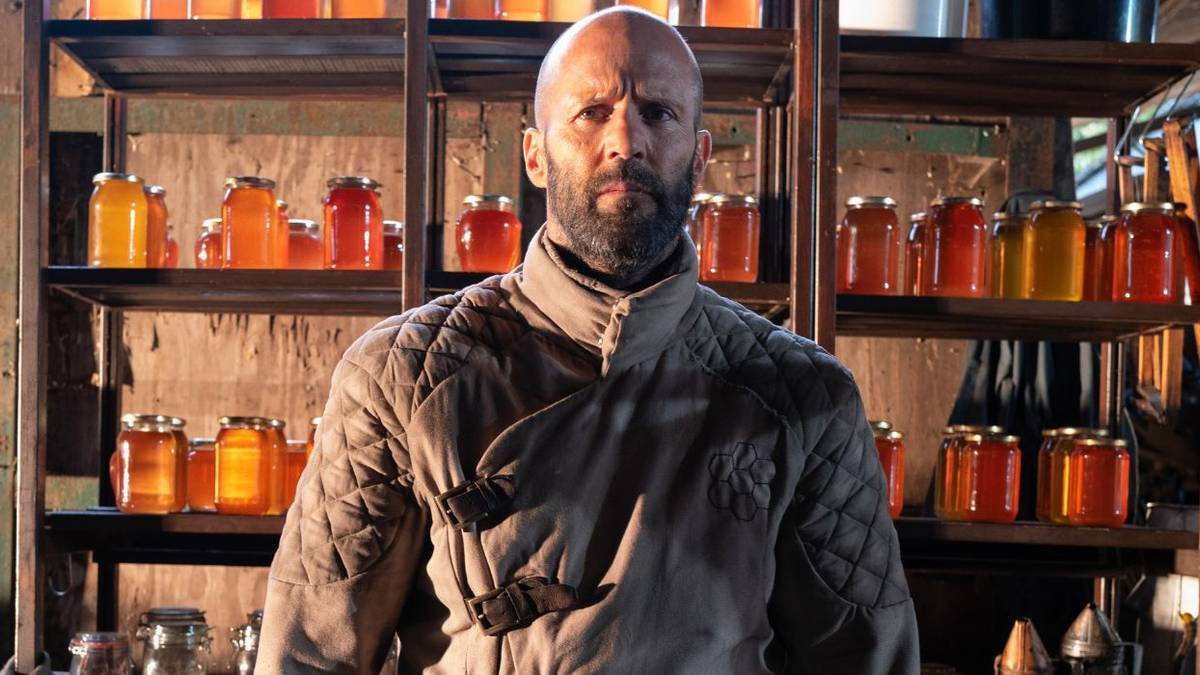 Jason Statham as Adam Clay, standing in front of jars of honey, in The Beekeeper