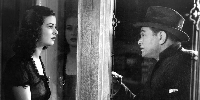 A woman looks out her rain-streaked window at a man pressing his face against the glass.