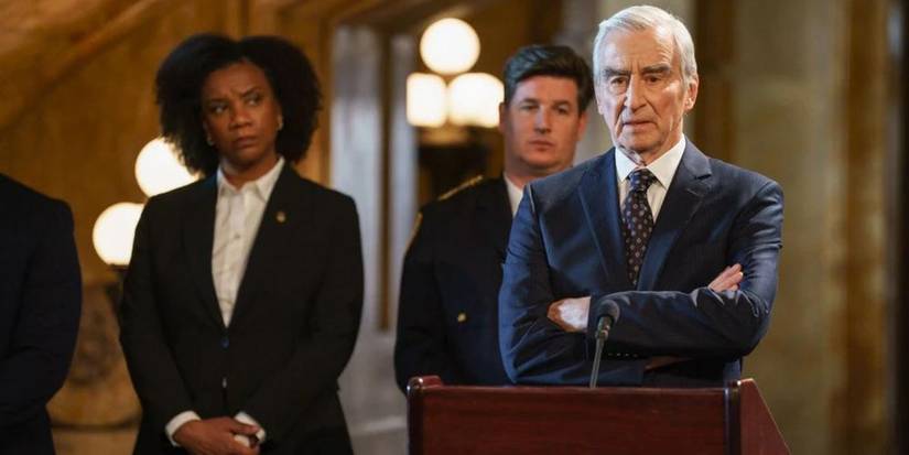 A man with his arms folded at a podium as a woman and other man look on in Law & Order.