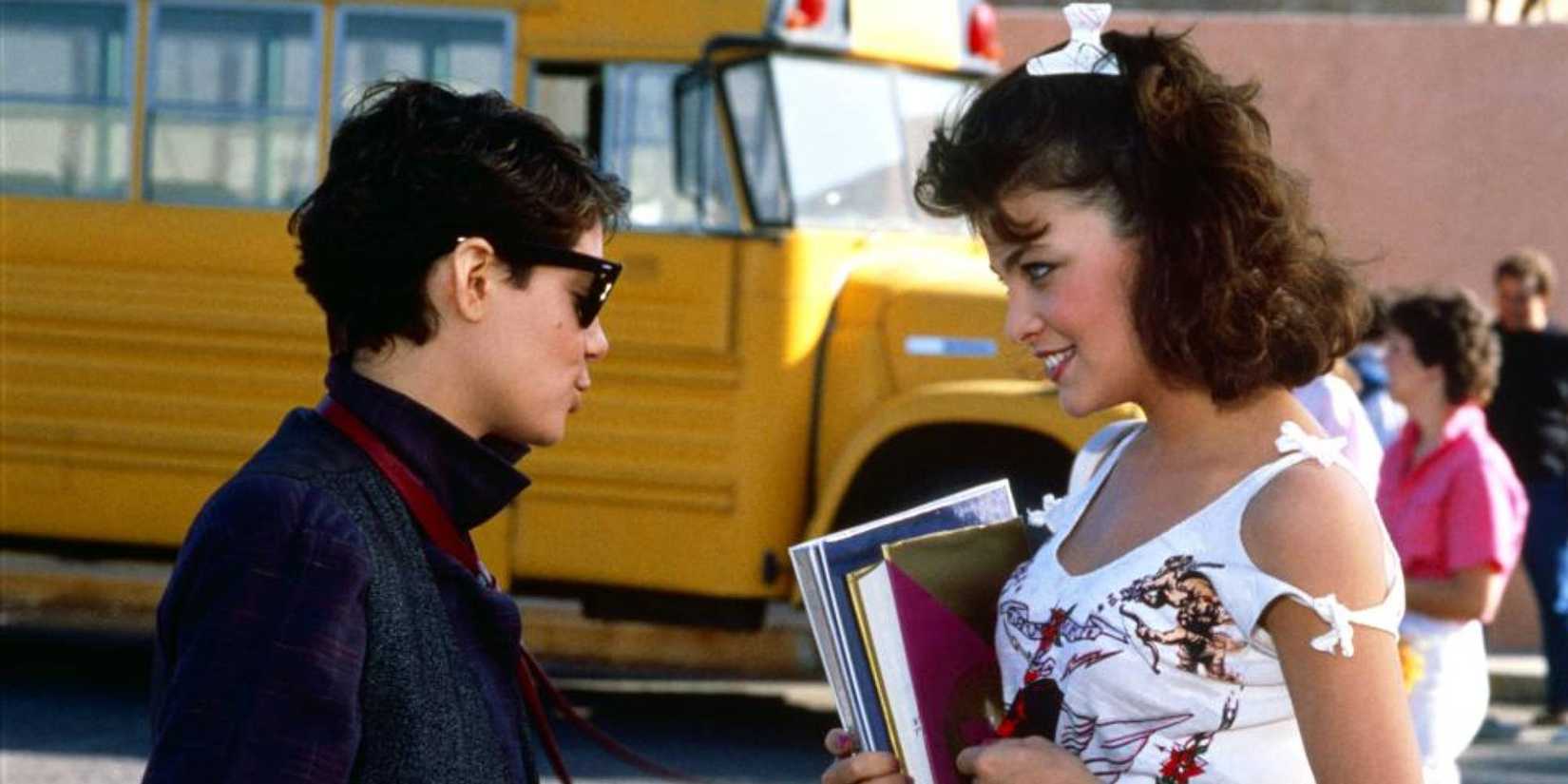 Joyce Hyser posing as a teen boy talking to a teen girl outside school in Just One of the Guys.