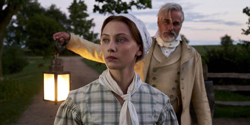 Grace Marks standing on a country road with Thomas Kinnear standing behind her holding a lamp with his raised arm, in Alias Grace