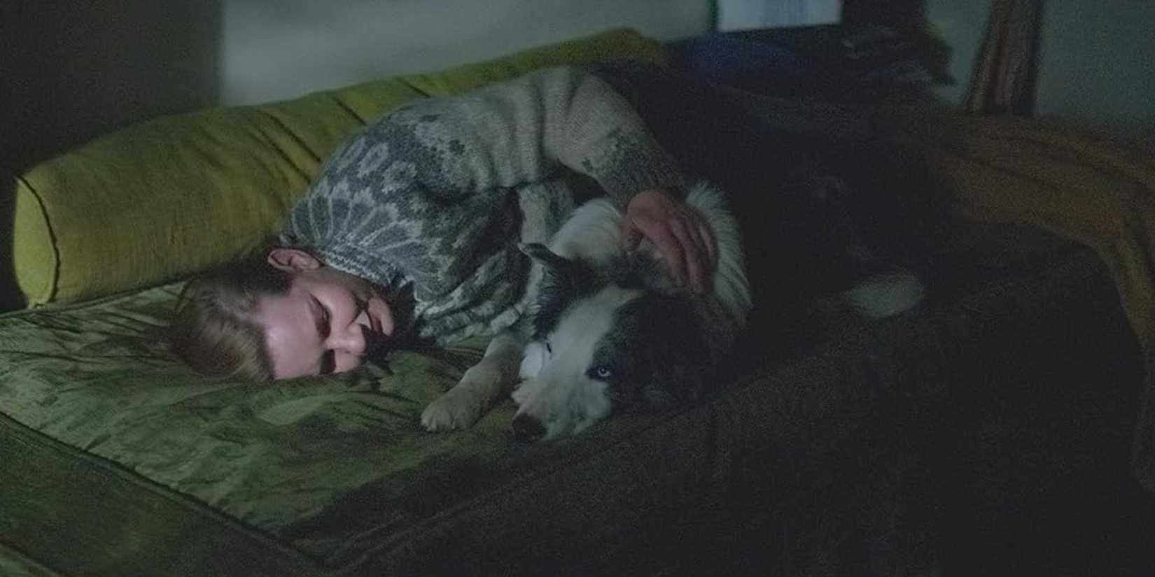 Sandra Voyter, lying on a sofa in a dark room and hugging her dog in Anatomy of a Fall