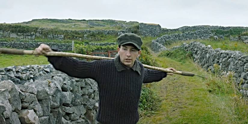 Barry Keoghan as Dominic, carrying a gardening tool through the countryside in The Banshees of Inisherin