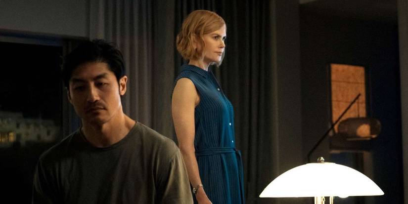 Brian Tee sitting in the bed while Nicole Kidman stands next to him in a blue dress in 'Expats'