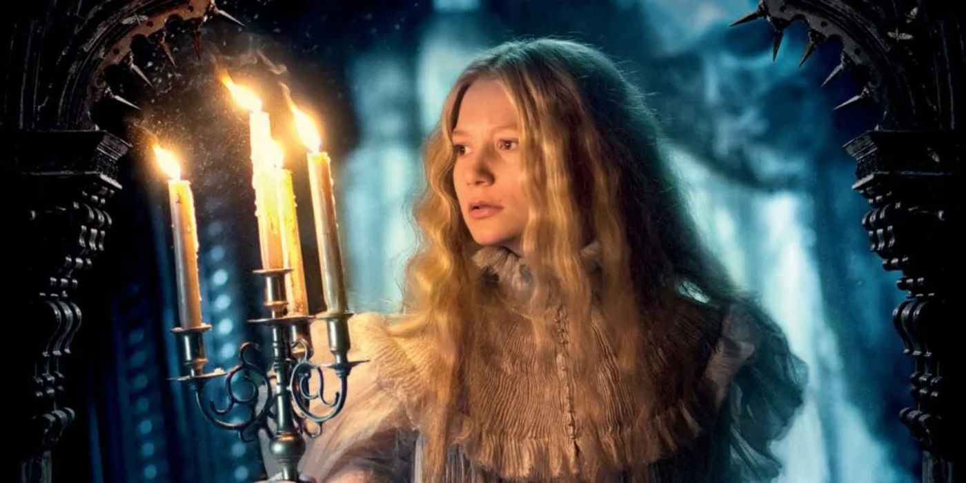 Mia Wasikowska in 'Crimson Peak' as Edith carries a lit candelabra in a darkened hall