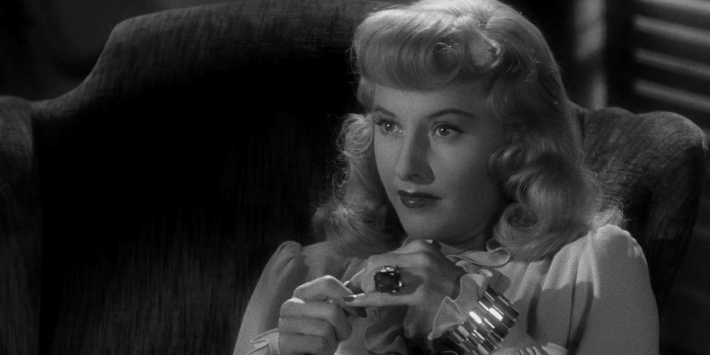 A close up of Phyllis Dietrichson, played by Barbara Stanwyck, staring intently offscreen to the left and pressing some of her fingers together in Double Indemnity