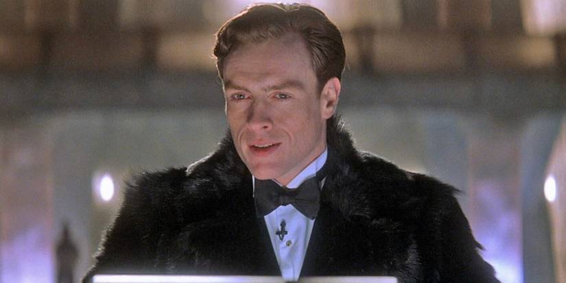 A man in a tuxedo and a black fur coat stands on a podium giving a speech.