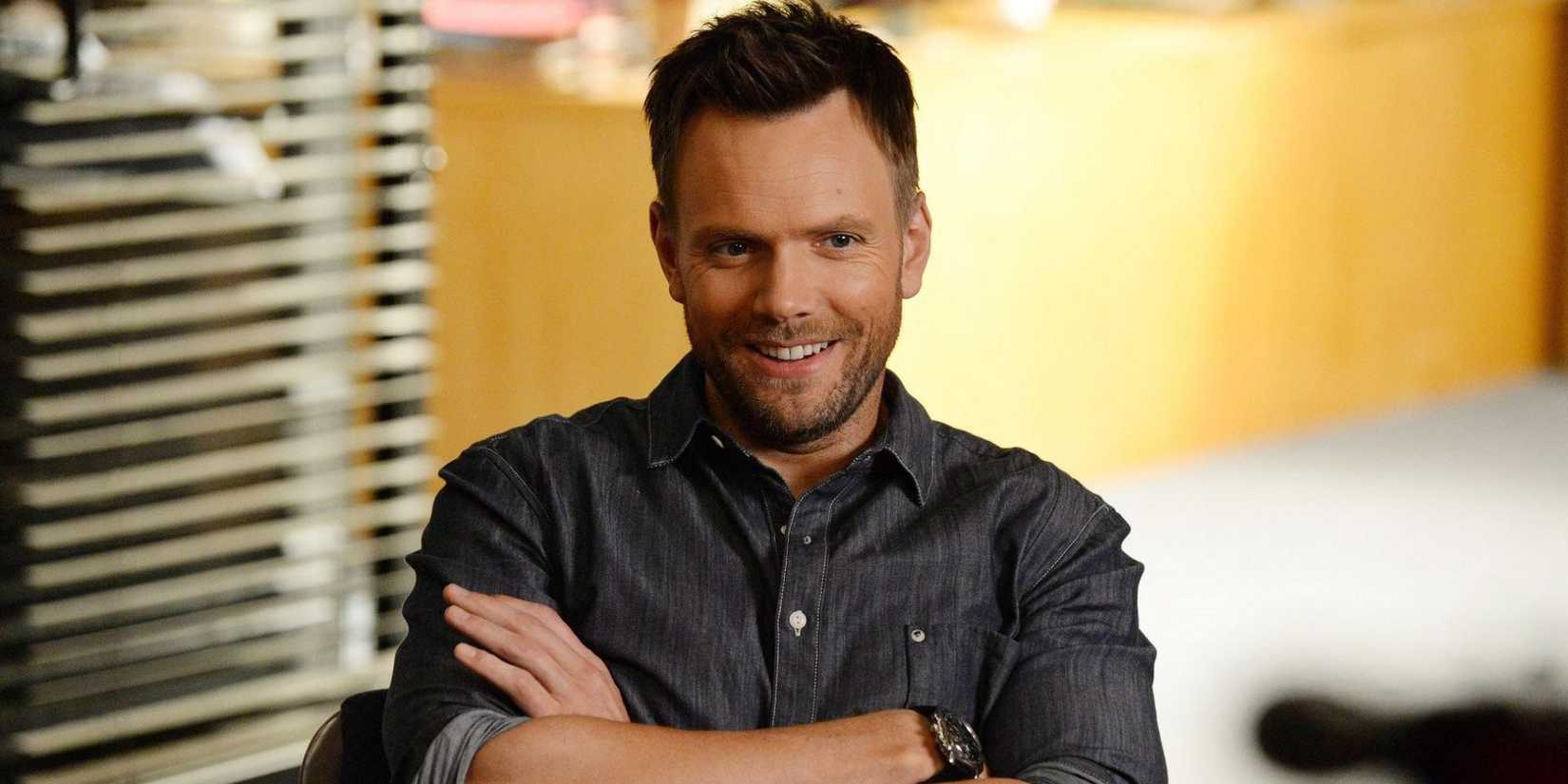 Jeff Winger (Joel McHale) from Community sitting with hands folded, smiling