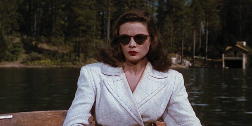 Ellen, played by Gene Tierney, wearing a white blazer jacket and dark sunglasses, sitting in a boat on the lake and staring ahead with a cold blank expression, in Leave Her to Heaven
