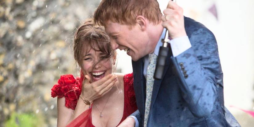 Mary (Rachel McAdams) and Tim (Domhnall Gleeson) laughing under an umbrella in the rain in About Time.
