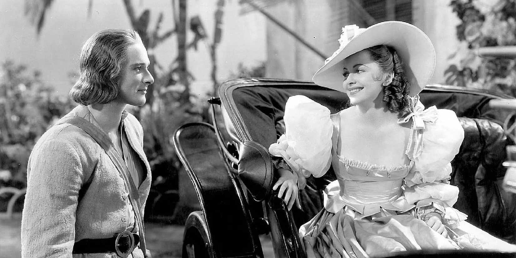 Olivia de Havilland and Errol Flynn in Captain Blood looking at each other while smiling.