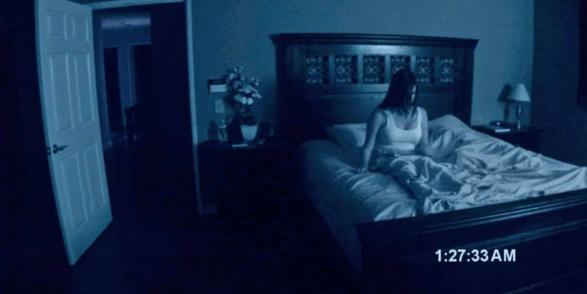 A nighttime camera captures a woman sitting up in bed in Paranormal Activity
