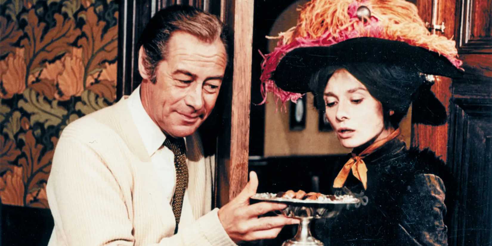 Professor Henry Higgins (Rex Harrison) offers Eliza Doolittle (Audrey Hepburn) a tray of food in My Fair Lady