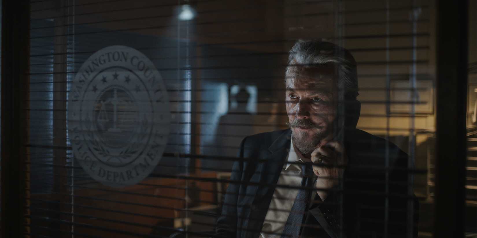Tommy Flanagan on the phone behind a window in a police station in Sleeping Dogs