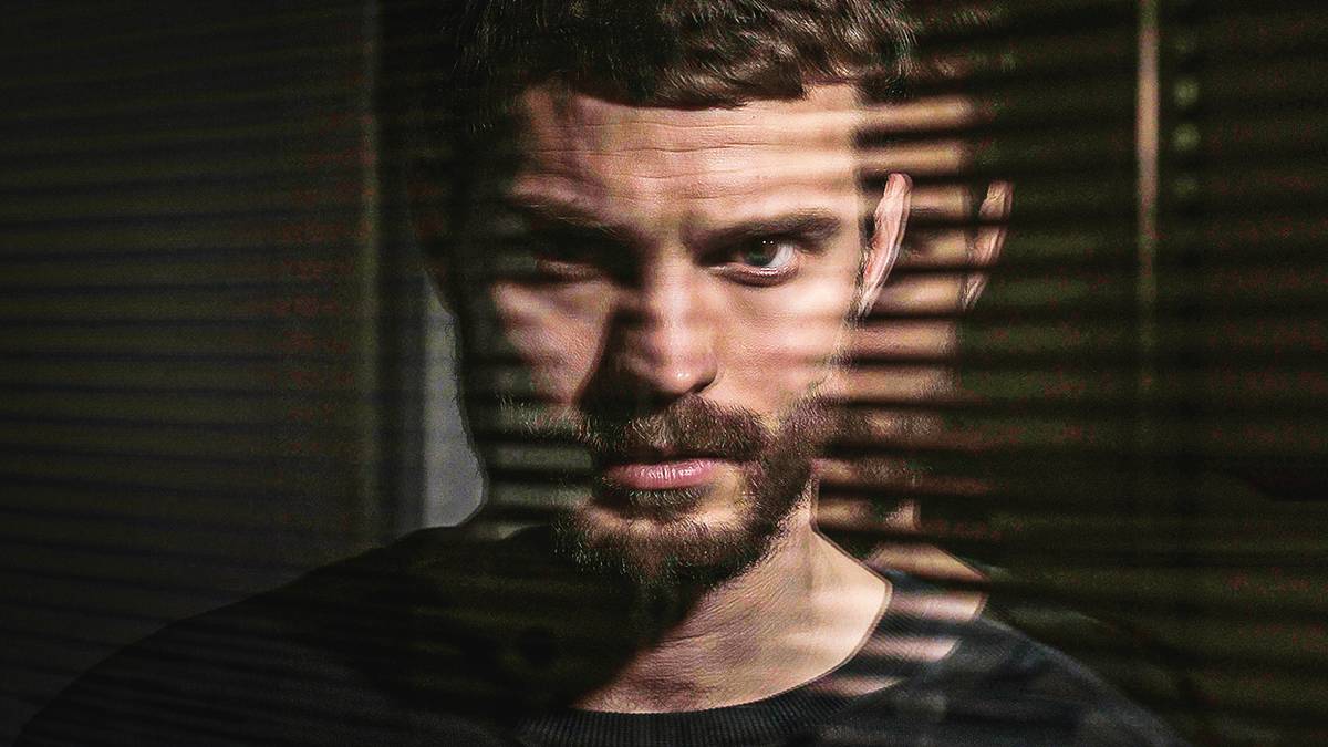 A publicity still of Jamie Dornan in The Fall, staring straight into the camera with a double effect behind him and shadows cast by window blinds over his face