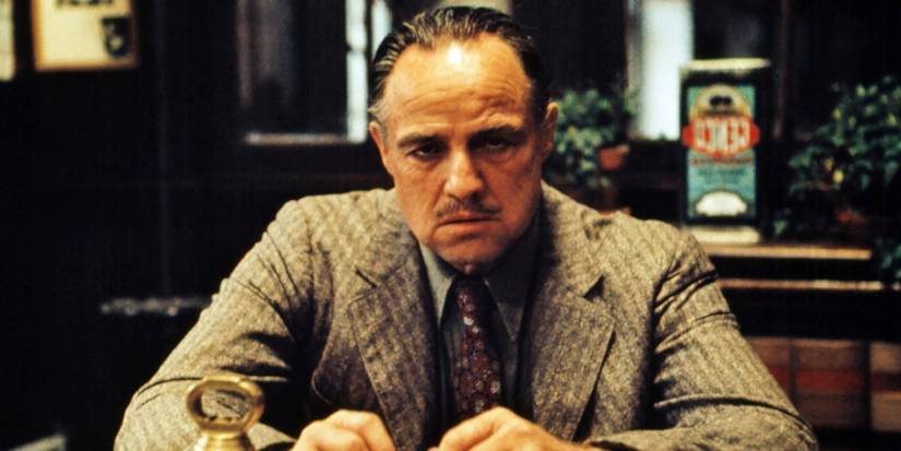 Marlon Brando as Vito Corleone, sitting down at a table alone in a restaurant in The Godfather