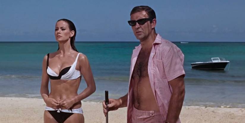 Bond stands on a beach in a pink shirt with a harpoon gun alongside Domino in Thunderball